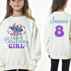 Puede incluir: Sudadera de color crema con un personaje de dibujos animados y las palabras "Birthday Girl" en azul y morado. La parte trasera de la sudadera tiene el nombre "Jennie" en escritura azul y el n&uacute;mero "8" en morado.