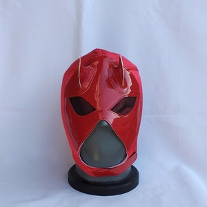 Puede incluir: Máscara de lucha libre roja con cuernos blancos y una zona de ojos de malla negra.