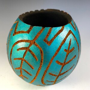 May include: A teal blue ceramic pot with a brown leaf design. The pot has a wide opening and a rounded shape.