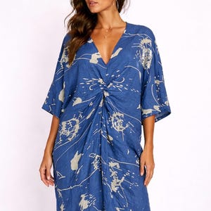 May include: A blue dress with a V-neck and short sleeves. The dress features a twist detail at the waist and a white and beige splatter pattern. The fabric appears lightweight and flowing, suitable for warm weather.
