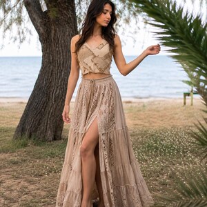May include: A beige two-piece set consisting of a sleeveless crop top with a patchwork texture and a matching floor-length tiered maxi skirt featuring intricate lace panels and a high front slit with an adjustable drawstring waist detail.