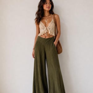 May include: A beige crochet halter crop top with a ruffled hem and a front tie closure, paired with olive green wide-leg trousers featuring a high waistband and side pockets, accompanied by a brown woven shoulder bag and brown sandals.
