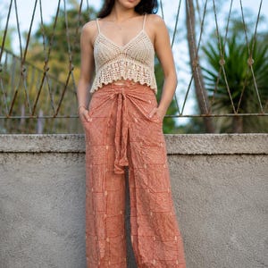 May include: A beige crochet camisole top with thin straps and a scalloped hem paired with wide-leg trousers featuring a rust-orange and white geometric line pattern, a high-waisted tie-front closure, and side pockets in a loose-fitting silhouette.