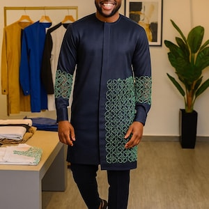 May include: A navy blue long-sleeved tunic featuring a mandarin collar and a vertical panel of intricate green geometric embroidery on the front and sleeves, paired with matching navy blue trousers and black strappy sandals.
