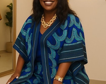 May include: A blue and teal patterned kimono-style jacket worn over a matching blue top and trousers. The jacket features a repeating semi-circular graphic print with striped trim along the edges. A chunky gold chain necklace and a gold bracelet are worn.