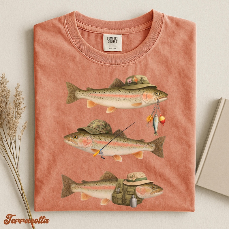 Terracotta Comfort Colors® shirt flat lay showing three rainbow trout with detailed fishing gear like camo hats, vest, and tackle.