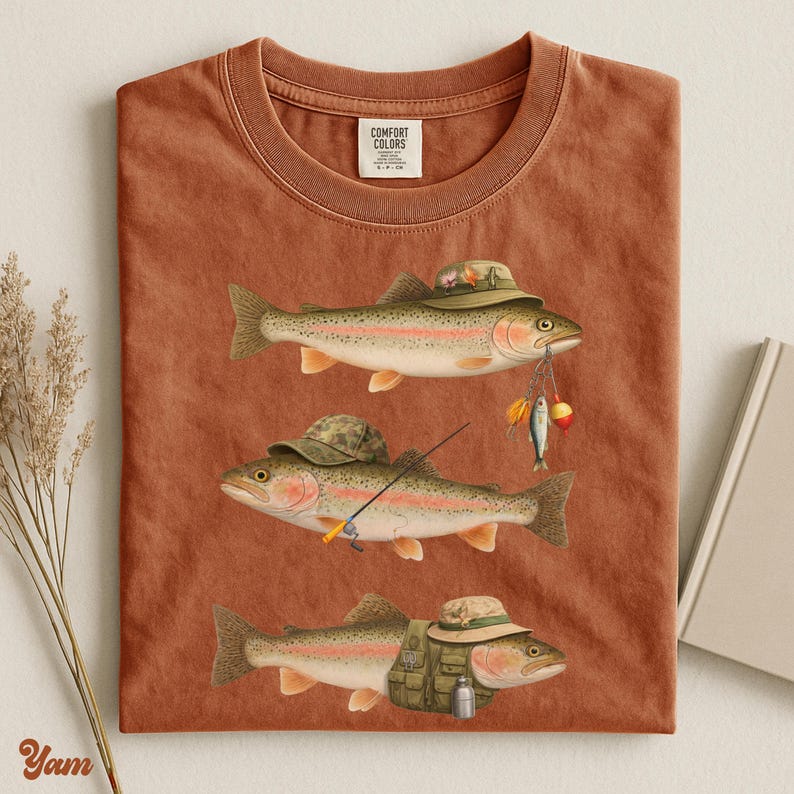 Yam Comfort Colors® flat lay shirt featuring three trout with fishing gear, camo hats, lures, and a vest. Ideal for outdoorsy gifts.