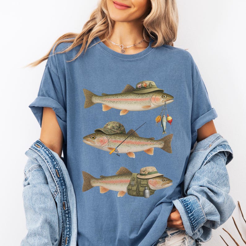 Woman wearing blue jean Comfort Colors® shirt featuring three trout illustrated with fisherman hats, lures, rod, and fishing vest.