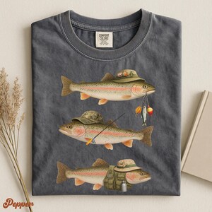 Pepper Comfort Colors® shirt folded flat, featuring illustrated trout wearing fisherman hats, holding bait, rod, and a green vest.