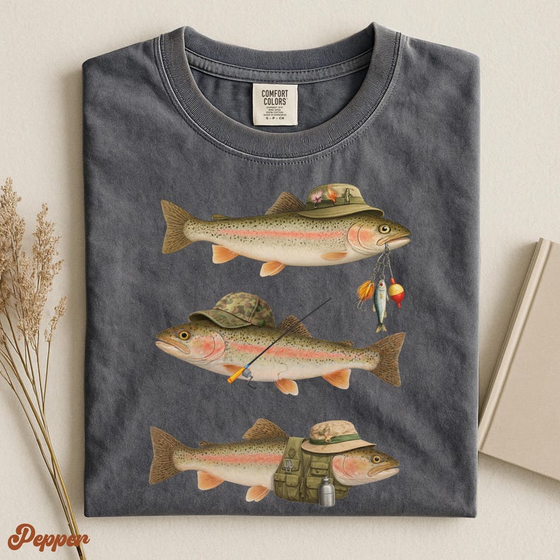 Pepper Comfort Colors® shirt folded flat, featuring illustrated trout wearing fisherman hats, holding bait, rod, and a green vest.