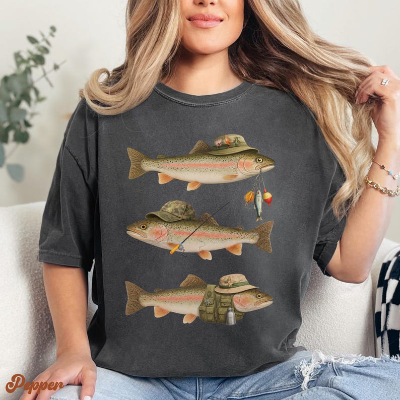 Woman wearing pepper Comfort Colors® shirt with three trout dressed in fishing gear, including hats, rod, vest, and bait accessories.