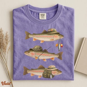 Violet Comfort Colors® shirt laid flat, printed with three trout dressed as fishermen, including hats, tackle, and a fishing vest.