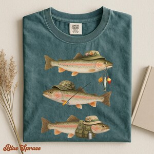 Blue spruce Comfort Colors® shirt folded flat, showing three trout dressed in full fishing gear: camo hats, vest, rod, and lures.