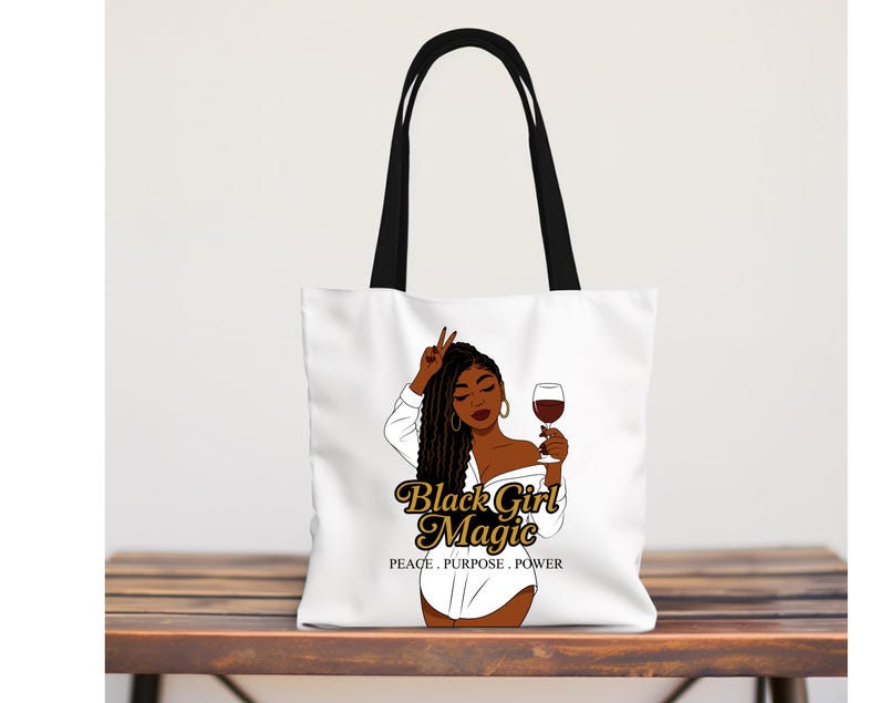 Puede incluir: Bolso tote blanco con asas negras. Presenta un gr&aacute;fico de una mujer negra sosteniendo una copa de vino y haciendo el signo de la paz. El texto "Black Girl Magic" est&aacute; en oro, con "PEACE. PURPOSE. POWER" debajo.