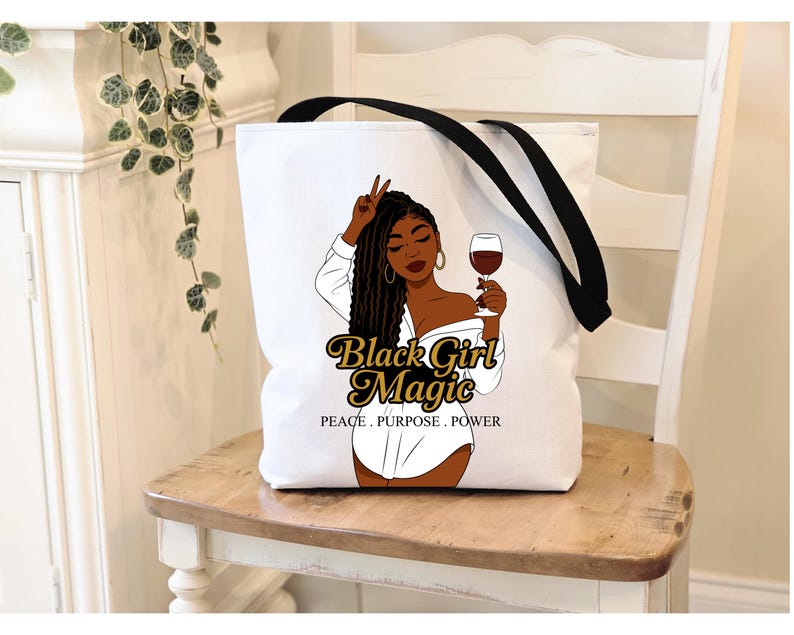 Puede incluir: Bolso tote blanco con correas negras. Presenta un gr&aacute;fico de una mujer negra sosteniendo una copa de vino. El texto "Black Girl Magic" est&aacute; en oro, con "PEACE. PURPOSE. POWER" debajo.