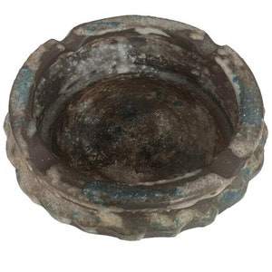 Puede incluir: Un cenicero redondo de cerámica marrón con un esmalte azul y blanco. El cenicero tiene un borde ligeramente elevado y una superficie texturizada.