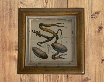 May include: A framed print of a vintage illustration of a scale with the word "LIBRA" on a ribbon. The scale is made of metal and has two pans. The print is in a gold frame with a white mat.