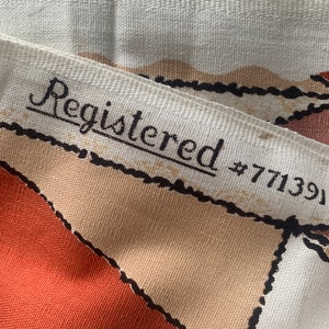 Peut inclure: Gros plan sur un tissu blanc avec un motif g&eacute;om&eacute;trique brun et orange. Le tissu a une bordure noire et le texte "Registered #771391" est imprim&eacute; sur le tissu.