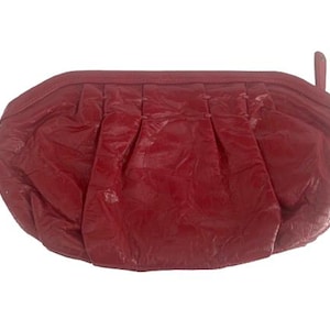 May include: A red, oval-shaped clutch purse with a gathered design. The purse has a textured appearance and a small loop on one end. The overall style is vintage.