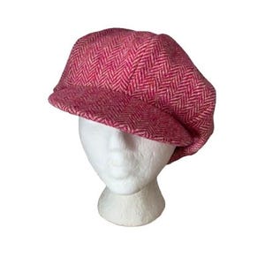Puede incluir: Gorra estilo newsboy rosa con estampado de espiga. La gorra se muestra sobre una cabeza de maniquí blanca. Presenta una corona redondeada y una pequeña visera rígida. La tela tiene una apariencia texturizada.