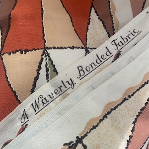 Peut inclure: Gros plan sur un tissu blanc avec un motif g&eacute;om&eacute;trique brun, beige et orange. Le tissu porte une &eacute;tiquette indiquant "A Waverly Bonded Fabric".