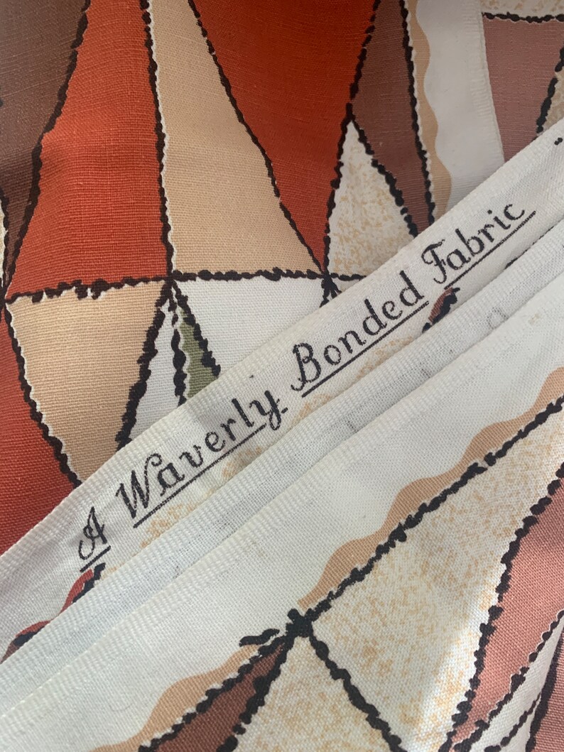 Peut inclure: Gros plan sur un tissu blanc avec un motif g&eacute;om&eacute;trique brun, beige et orange. Le tissu porte une &eacute;tiquette indiquant "A Waverly Bonded Fabric".