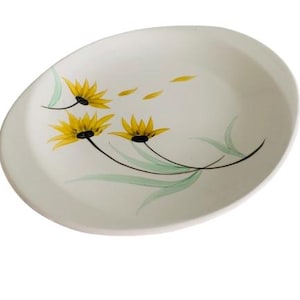 May include: Oval-shaped, off-white ceramic serving platter with a floral design. The platter features yellow flowers with black centers and green leaves. The flowers are painted with delicate brushstrokes, adding a touch of elegance to the piece.