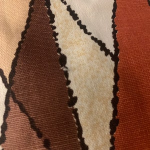 Peut inclure: Gros plan sur un tissu avec un motif g&eacute;om&eacute;trique dans les tons de brun, beige et orange. Le tissu a une surface textur&eacute;e et une apparence l&eacute;g&egrave;rement d&eacute;lav&eacute;e.