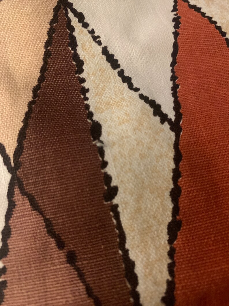 Peut inclure: Gros plan sur un tissu avec un motif g&eacute;om&eacute;trique dans les tons de brun, beige et orange. Le tissu a une surface textur&eacute;e et une apparence l&eacute;g&egrave;rement d&eacute;lav&eacute;e.