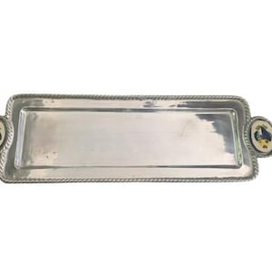 Pode incluir: Uma bandeja de servir prateada com uma borda de corda e duas alças decorativas de cerâmica azul e amarela.