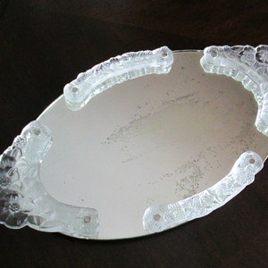 Peut inclure: Un miroir de toilette ovale avec un cadre en verre transparent. Le cadre est décoré d'un motif floral. Le miroir est parfait pour une coiffeuse ou une table de toilette.