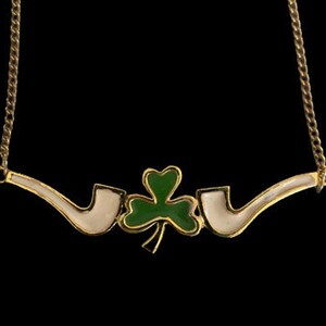 Può includere: Collana d'oro con un design a trifoglio bianco e verde. Il trifoglio è circondato da due pipe bianche.