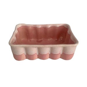 以下が含まれることがあります： 波状の縁が付いた長方形のセラミック皿。 皿は2色で、外側は薄いピンク色、内側は濃いピンク色です。 ベースには、一連の丸みを帯びたピンク色のスカラップがあります。