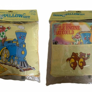 May include: Two yellow pillowcases with a book and pillow set theme. One pillowcase features a blue train with a red and white clown on top. The other pillowcase features two brown teddy bears. The text on the pillowcases reads "The Little Engine That Could Book & Pillow Set" and "The Easy-to-Read Little Engine That Could".