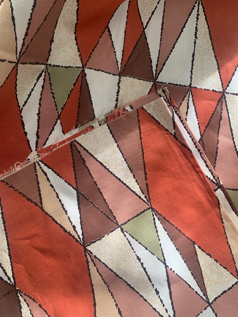 Peut inclure: Un tissu avec un motif g&eacute;om&eacute;trique de triangles dans des tons de brun, orange, vert et blanc. Le tissu a une surface textur&eacute;e.