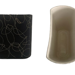 Puede incluir: Dos jarrones de cerámica, uno con un patrón de remolino negro y dorado y el otro blanco.