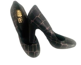 May include: A pair of black high-heeled pumps with a textured, grid-like pattern. The heels are thick and the shoes have a pointed toe. The interior of one shoe displays a gold logo with the letters "BF".