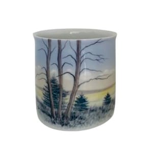 Puede incluir: Una taza de cerámica blanca con una escena pintada de árboles y una puesta de sol. Los árboles están desnudos y el cielo es azul claro con nubes amarillas.