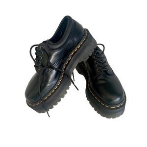 Può includere: Paio di scarpe platform in pelle nera con lacci neri e cuciture gialle. Le scarpe hanno una suola spessa e uno stile Oxford classico, adatte a vari outfit.