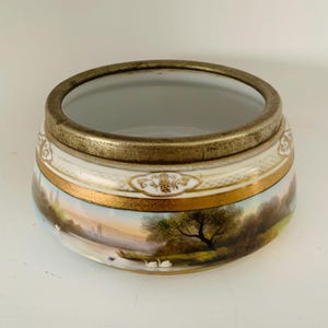 May include: A white porcelain bowl with a gold rim and a painted landscape scene. The bowl has a silver metal rim around the top.