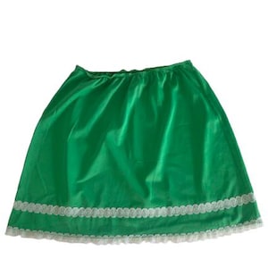 May include: A bright green skirt with an elastic waistband and a white lace trim along the hem. The skirt is made of a smooth, solid-colored fabric. The skirt is a simple, classic design.