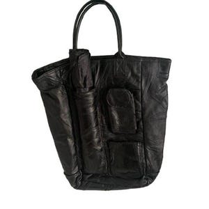 Puede incluir: Bolso tote de cuero negro con dos asas y múltiples bolsillos exteriores. El bolso tiene un diseño de patchwork y un bolsillo cilíndrico en el lateral. El bolso está hecho de cuero suave y texturizado.