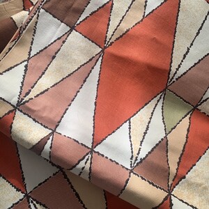 Peut inclure: Tissu avec un motif g&eacute;om&eacute;trique de triangles bruns, beiges et orange. Les triangles sont soulign&eacute;s de noir et ont un aspect textur&eacute;.