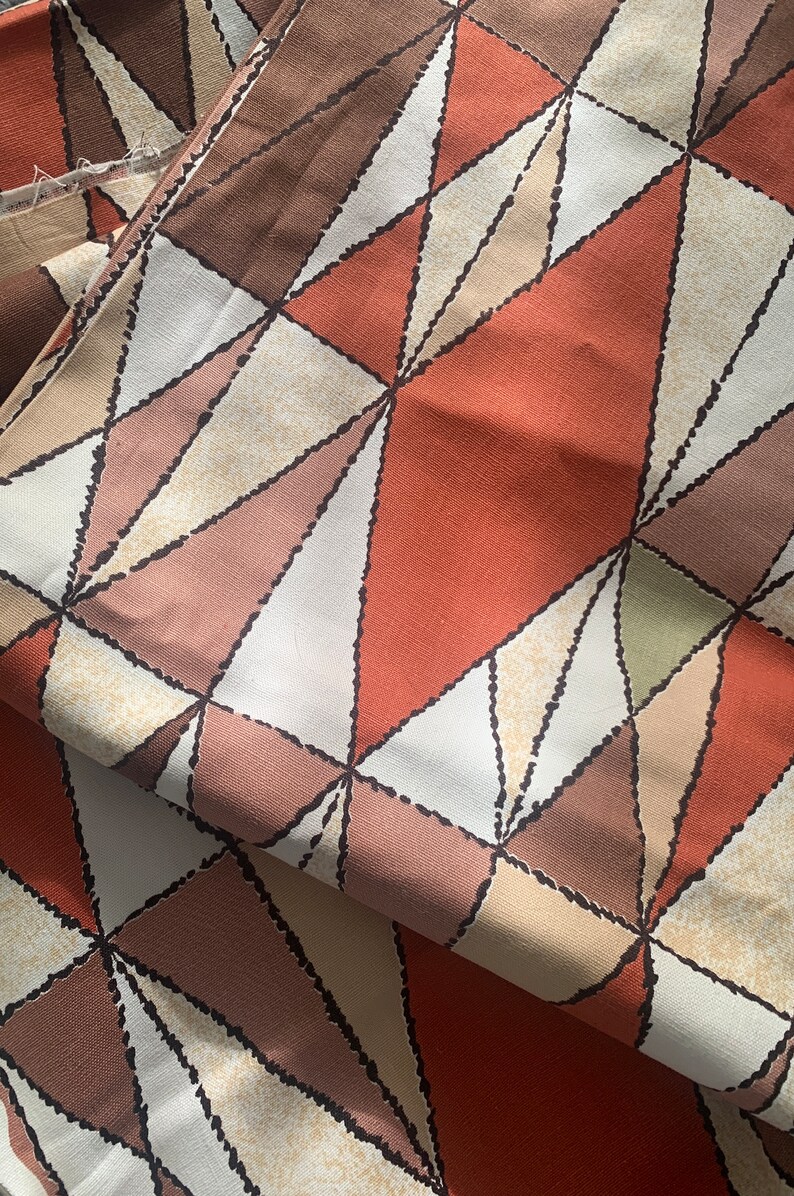 Peut inclure: Tissu avec un motif g&eacute;om&eacute;trique de triangles bruns, beiges et orange. Les triangles sont soulign&eacute;s de noir et ont un aspect textur&eacute;.