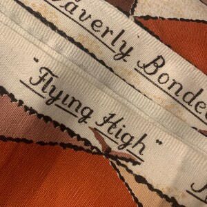 Peut inclure: Une &eacute;tiquette en tissu blanc avec du texte noir qui dit "Waverly Bonded "Flying High" ". L'&eacute;tiquette est sur un tissu &agrave; motifs brun et blanc.