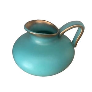 May include: A turquoise ceramic pitcher with a rounded body and a wide, open spout. The rim of the spout and the edges of the curved handle are finished with a metallic gold trim, providing a distinct contrast to the matte turquoise surface.