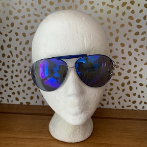 May include: Aviator sunglasses featuring a thin metallic frame with a blue brow bar and blue mirrored lenses. The lenses have a reflective surface showing a room interior. The sunglasses are displayed on a plain white mannequin head.
