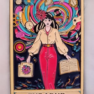 May include: A rectangular pin with a woman in a tan jacket and red trousers, holding a book and a bag with a flower. The background has colourful swirls, gears, and a clock. The text "THE ADHD" is at the bottom.