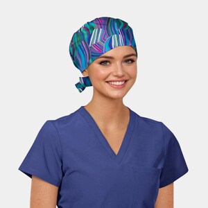 May include: A patterned surgical scrub cap featuring a vibrant design of blue, teal, purple, and white curved lines. The cap is tied at the back and worn with a blue V-neck scrub top.