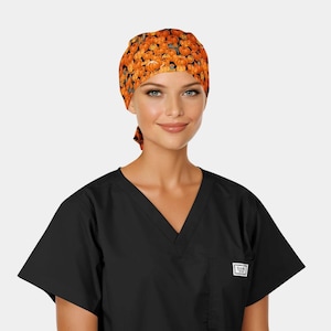May include: A black scrub top with a V-neck and a small pocket. The model is wearing a patterned scrub cap with orange pumpkins on a black background. The cap is tied in the back.